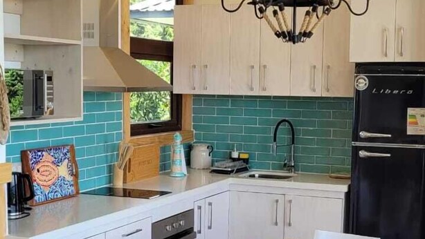 Una cocina moderna con armarios blancos, un refrigerador negro, una mesa de comedor de madera con sillas blancas y una araña.
