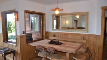 Une table à manger en bois, accompagnée de quatre chaises, un luminaire suspendu et un grand miroir placé au-dessus de la table.