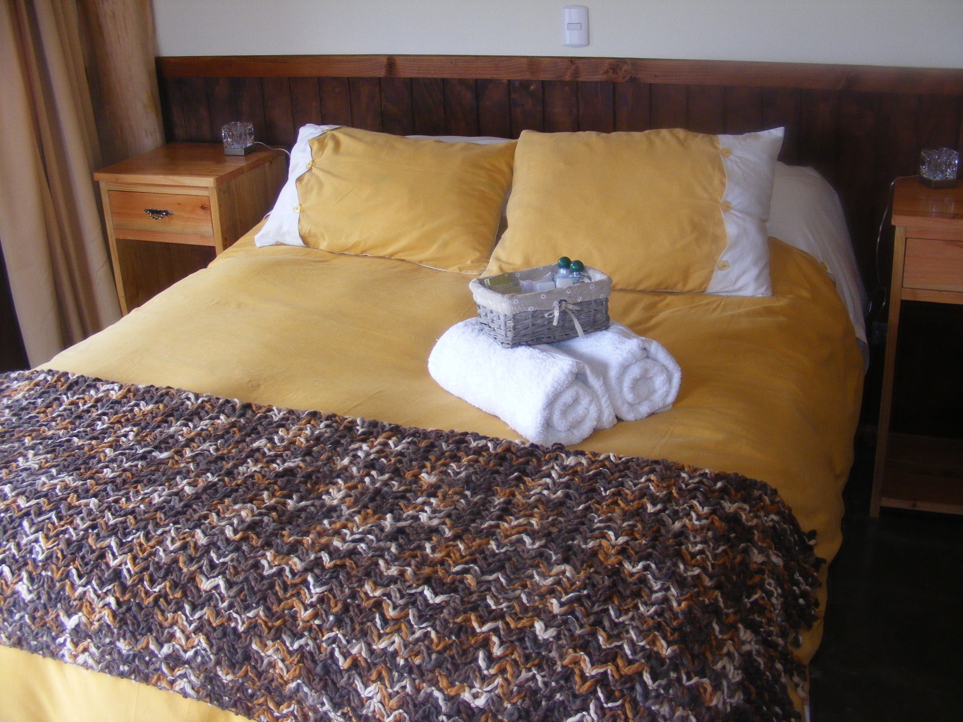 A hotel room with a large bed, two nightstands, a wooden headboard, and a woven throw blanket.