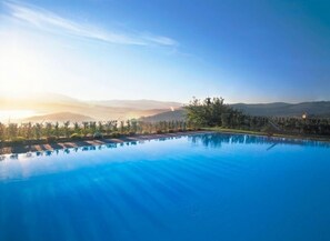 A serene swimming pool with clear blue water, surrounded by lush greenery and a backdrop of mountains. - Tenuta (San Casciano in Val di Pesa)