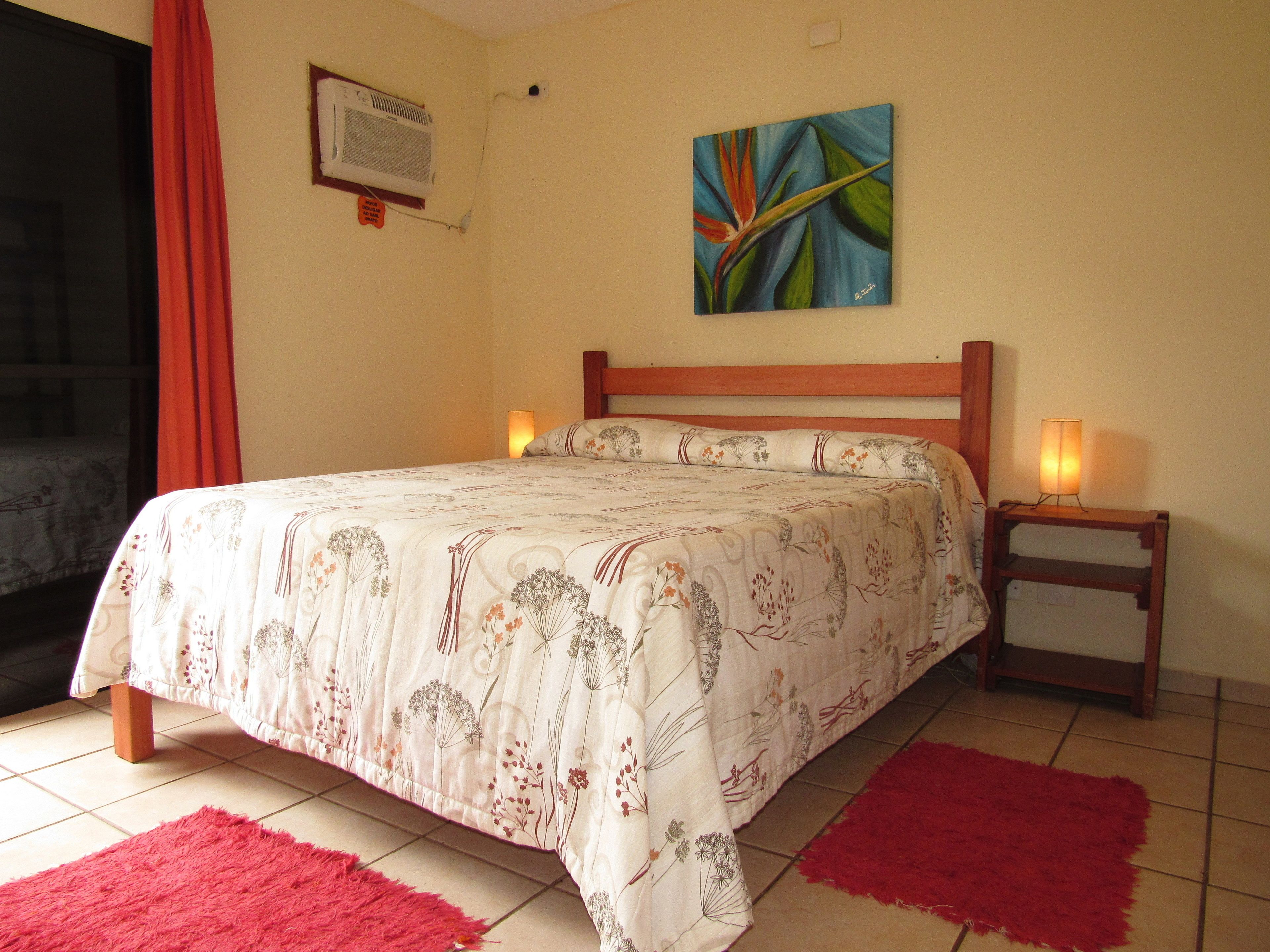 Quarto com cama, duas luminárias de cabeceira, um quadro na parede e uma janela com cortinas.