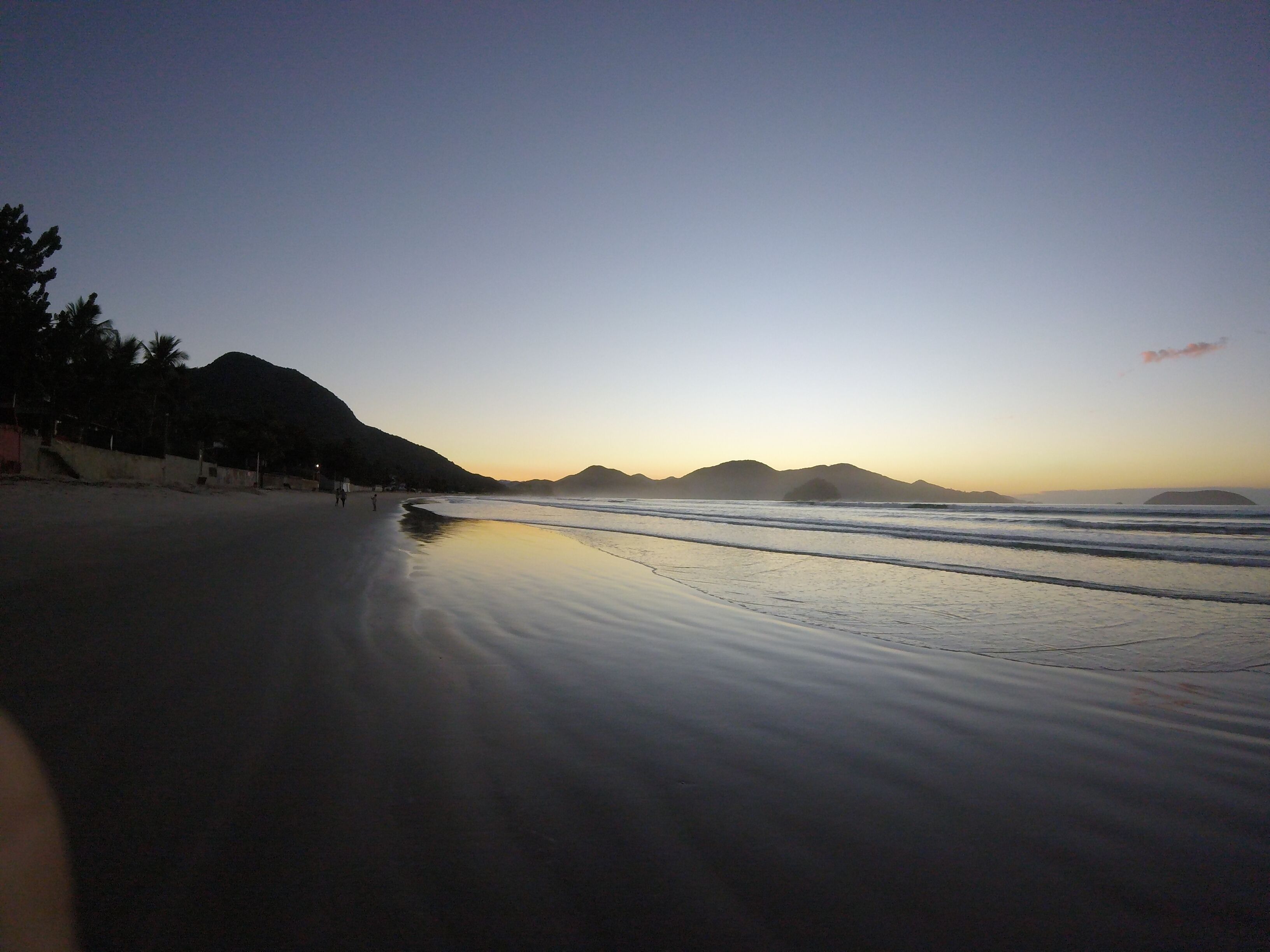 A beach with a calm sea, a mountain in the background, and a clear sky.