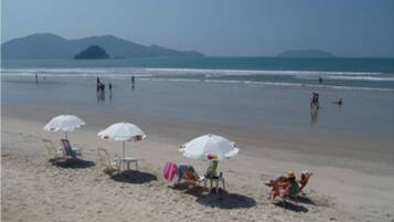Une plage avec des parasols blancs, des chaises longues et des gens dans l’eau.