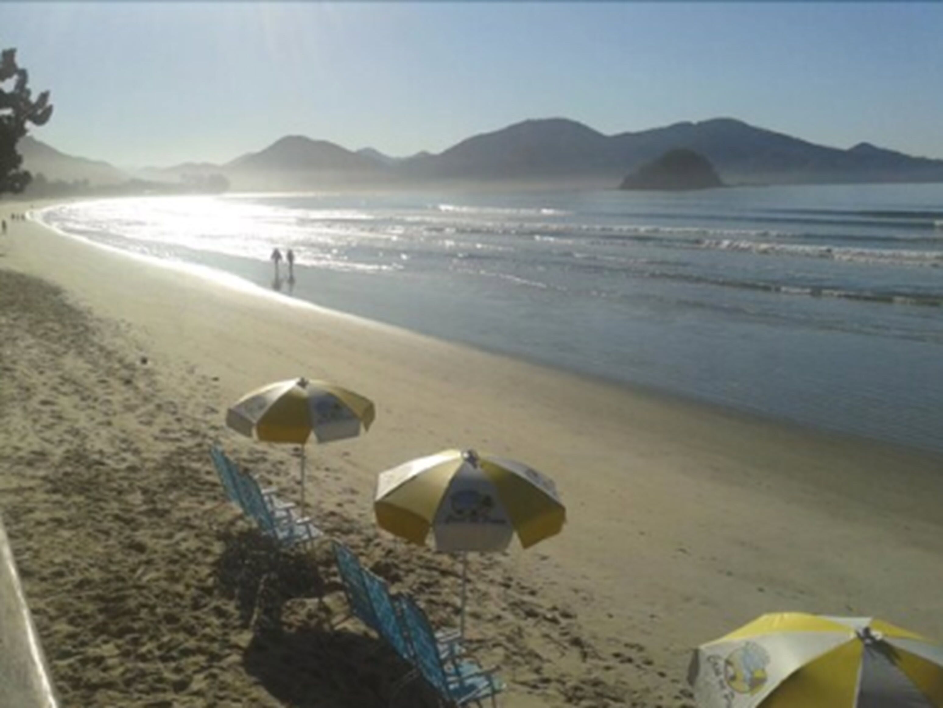 A beach with umbrellas and chairs, a clear sky, and mountains in the background.