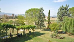 A garden with a table and chairs, a swing set, and a variety of trees. - Villa Cassia (Pienza)