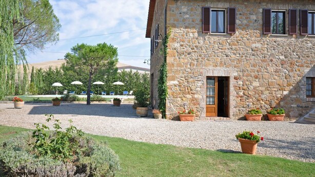 A stone building with a door and windows, surrounded by gravel and potted plants. - Villa Cassia (Pienza)