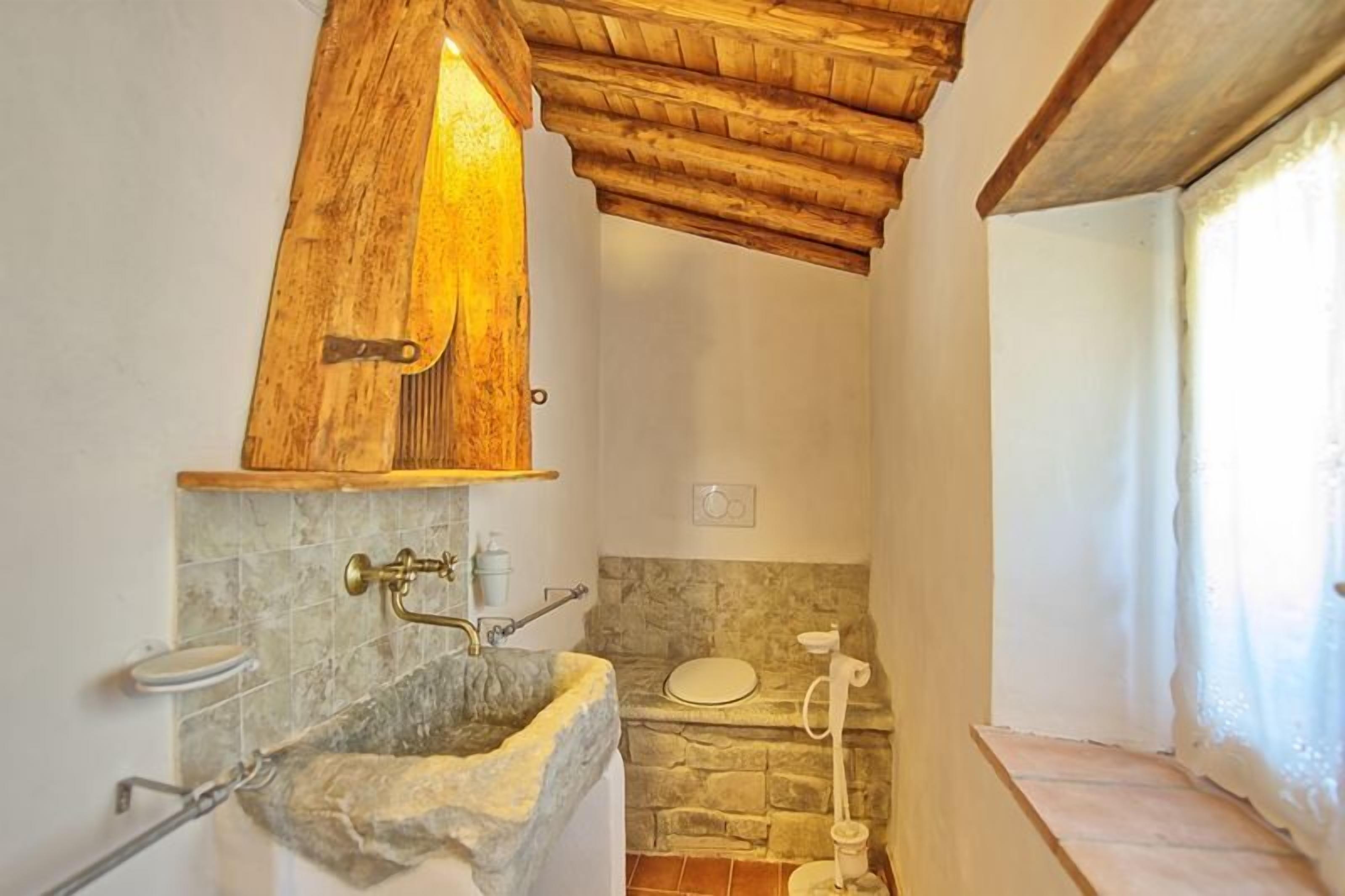 A bathroom with a stone sink, wooden vanity, and a rustic wooden ceiling.