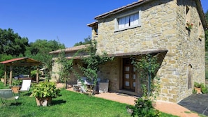 A stone house with a wooden door, a small porch with outdoor furniture, and a garden area. - Villa Margherita (Cortona)