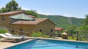A stone building with a swimming pool, lounge chairs, and a view of a mountainous landscape. - Villa Margherita (Cortona)