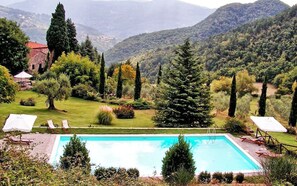 A rectangular pool with a clear blue water surface, surrounded by a well-maintained lawn and various trees. - Casa Uscioli (Pontassieve)