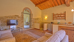 A cozy living room with a stone wall, a flat-screen TV, a wooden ceiling, and a kitchen area with a counter and sink. - Casa Uscioli (Pontassieve)