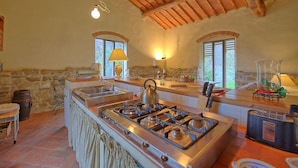 A rustic kitchen with a large island, stone walls, wooden beams, and a stone barrel. - Casa Uscioli (Pontassieve)