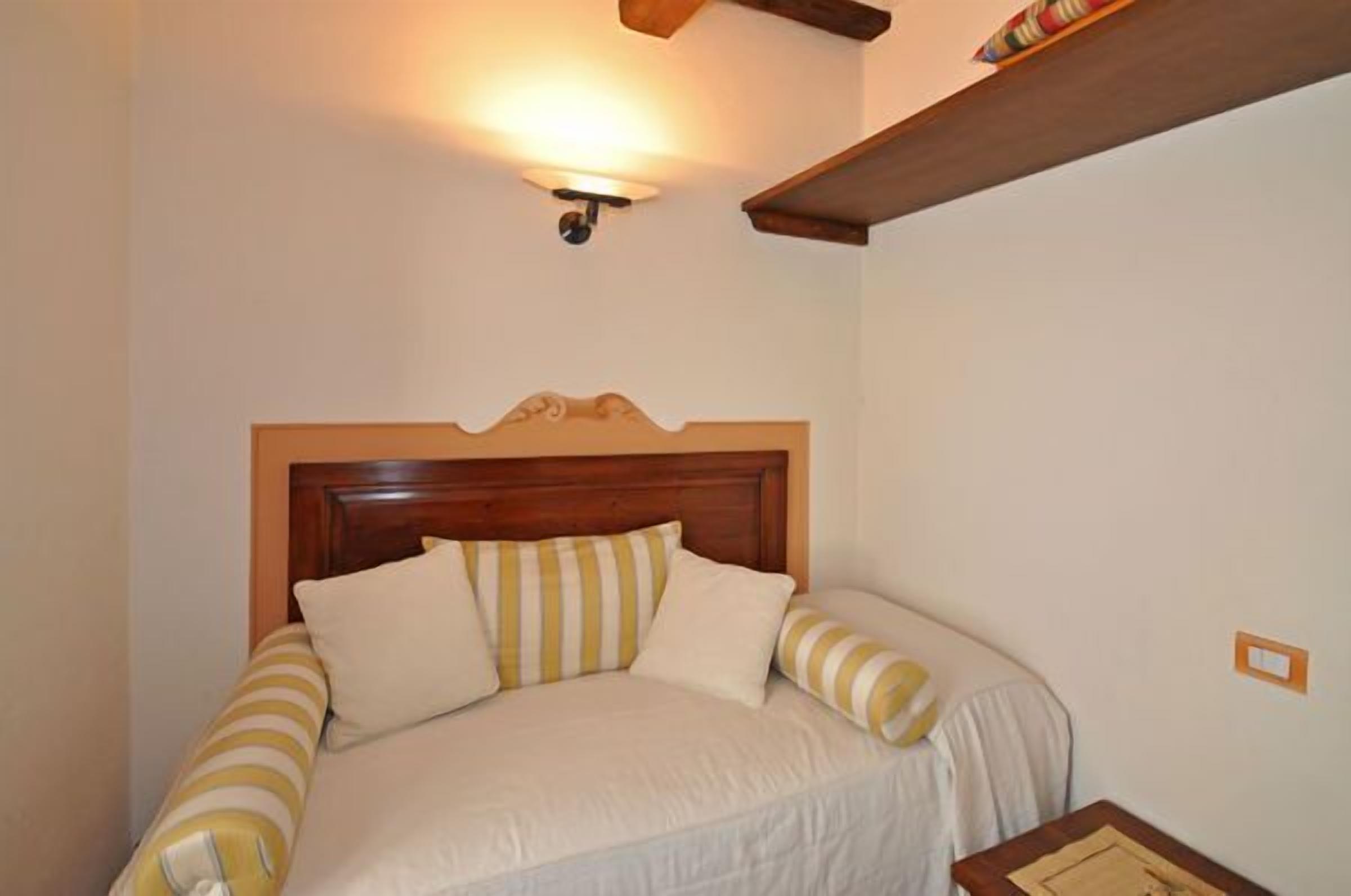 Une chambre avec une tête de lit en bois, un lit avec une literie à rayures, une table de chevet et un luminaire fixé au mur.