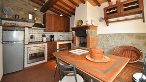 A rustic kitchen with wooden beams, a stone wall, a tiled backsplash, and a brick floor. - Villa Calcinaio (Cortona)