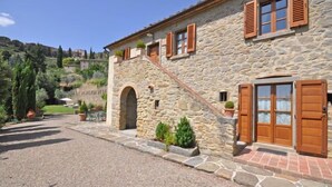 A stone building with wooden shutters, a central arched entrance, and a gravel driveway. - Villa Calcinaio (Cortona)