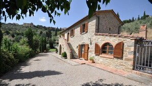 A stone house with a gravel driveway, wooden shutters, and a metal gate. - Villa Calcinaio (Cortona)