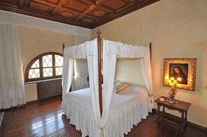 A four-poster canopy bed with a wooden headboard, a bedside table with a lamp, and a framed portrait on the wall. - Villa Guia (Bucine)