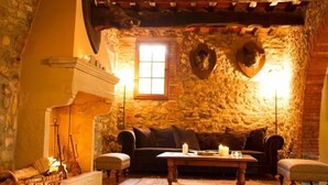 Una habitación con paredes de piedra, chimenea, un sofá, una mesa y un ventanal.
