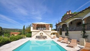 Un área de piscina con un mirador, sillas de descanso y un edificio de piedra con arcos.