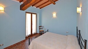 Un dormitorio con una cama, una silla, techo de madera y dos luces fijadas a la pared.