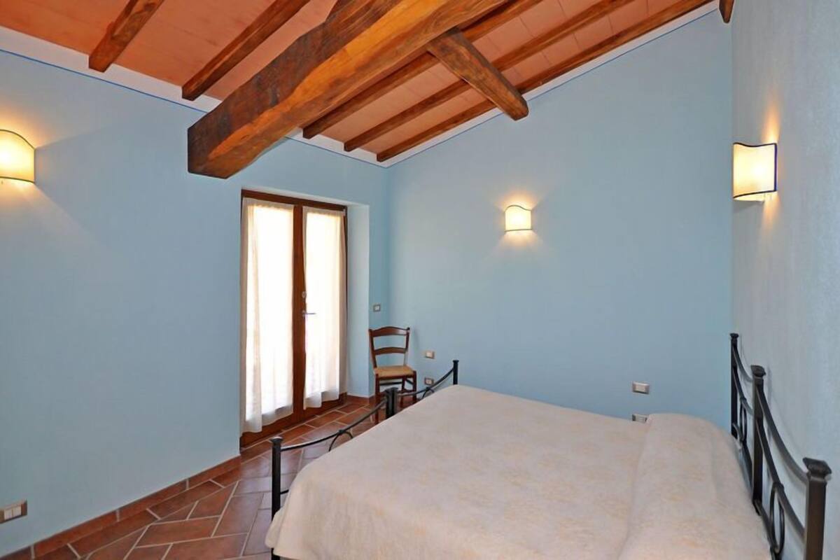 Una camera da letto con un letto, una sedia, soffitto in legno e due luci a parete.