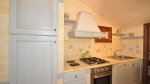 Una cocina con armarios blancos, estufa a gas, pileta y campana extractora.