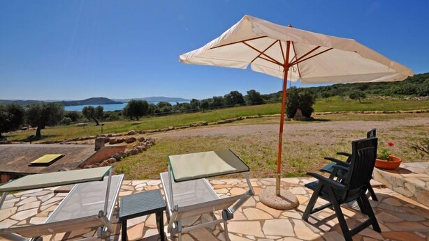 Un espacio al aire libre con mesas y sillas, un paraguas grande y vistas panorámicas del campo y un lago.