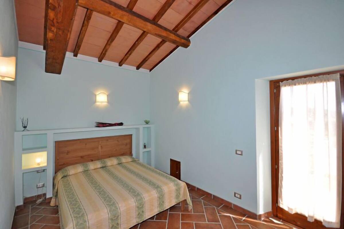 Una camera da letto con soffitto in legno, un letto con copripiumino a righe, due lampade a parete e una finestra con tende.
