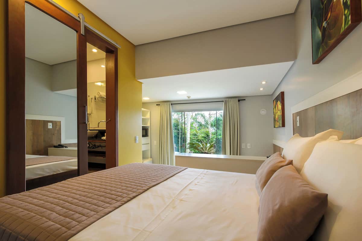 A hotel room with a large bed, a desk, a mirror, and a window with curtains.