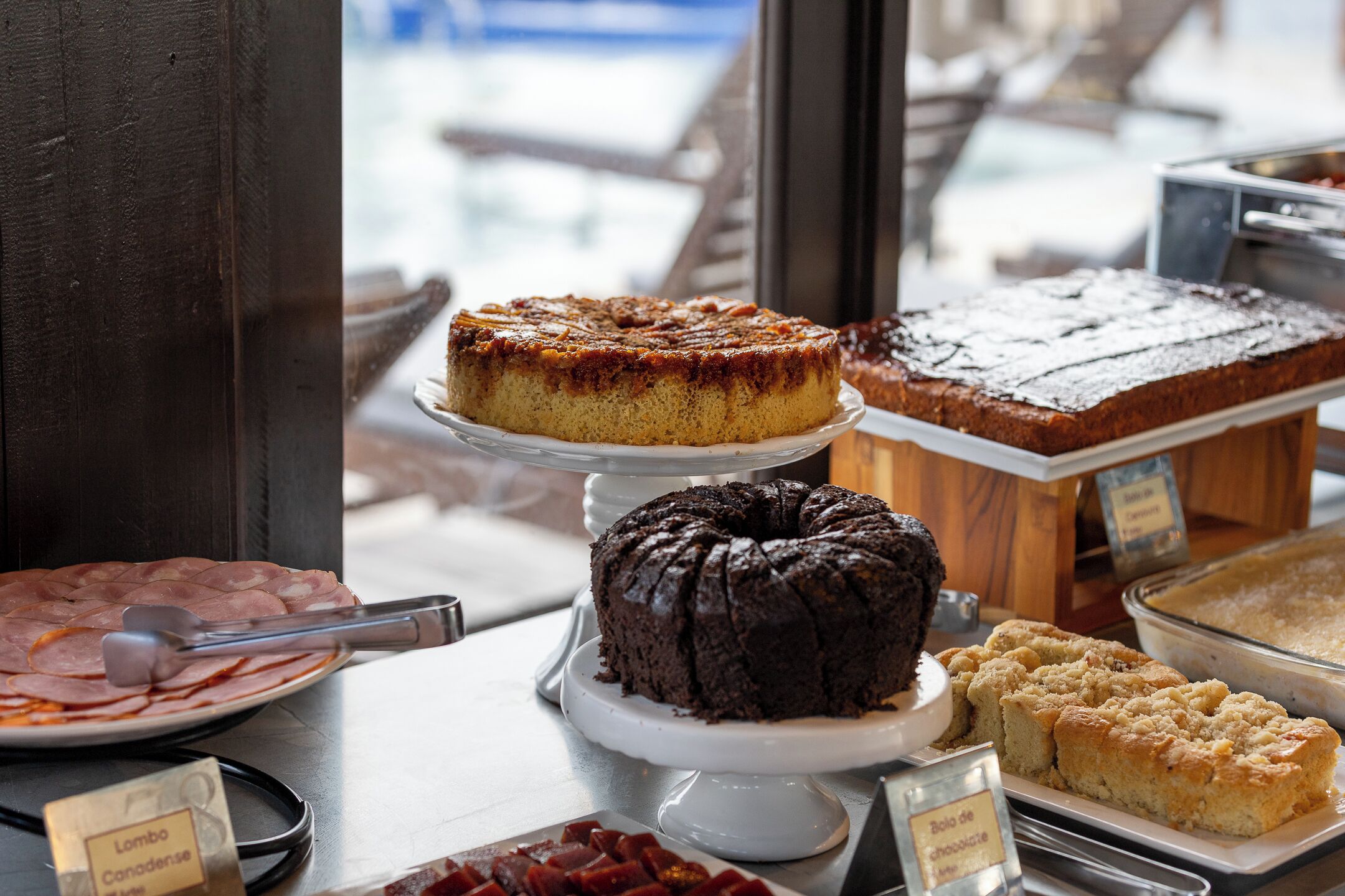 A variety of cakes and pastries displayed on a counter with a window in the background.