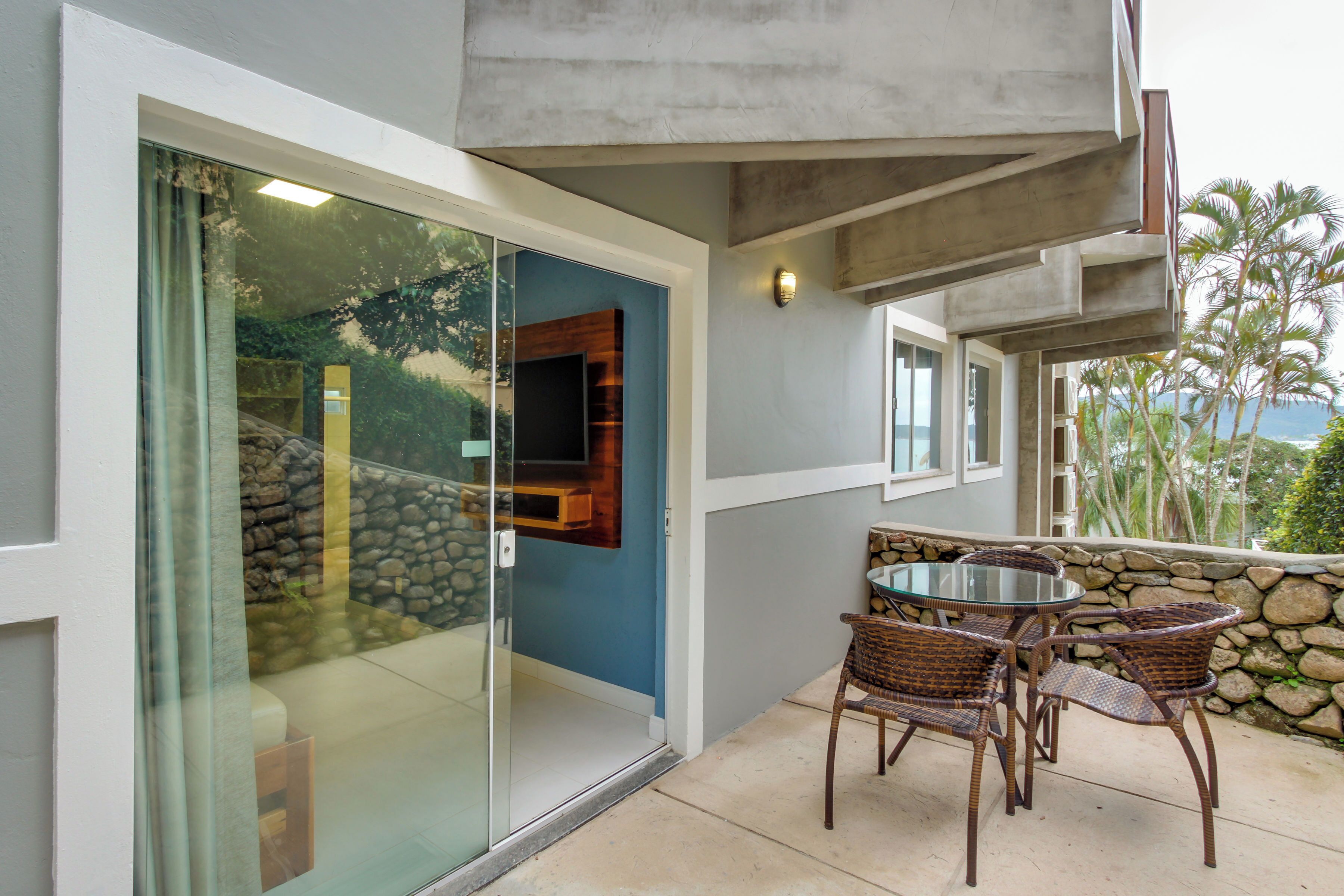 A modern outdoor patio with a glass door leading to a stone wall, wicker chairs, and a small table.