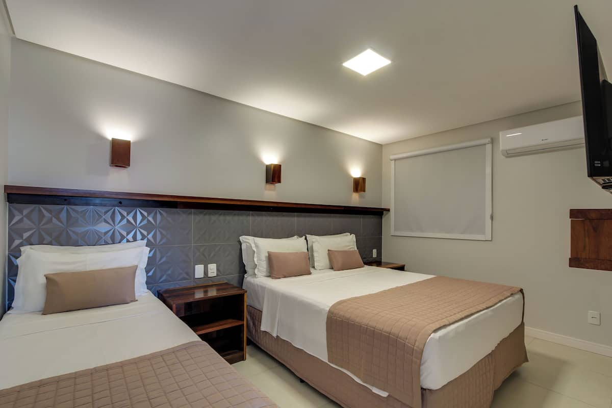 A hotel room with two beds, a wooden headboard, wall-mounted sconces, and an air conditioning unit.