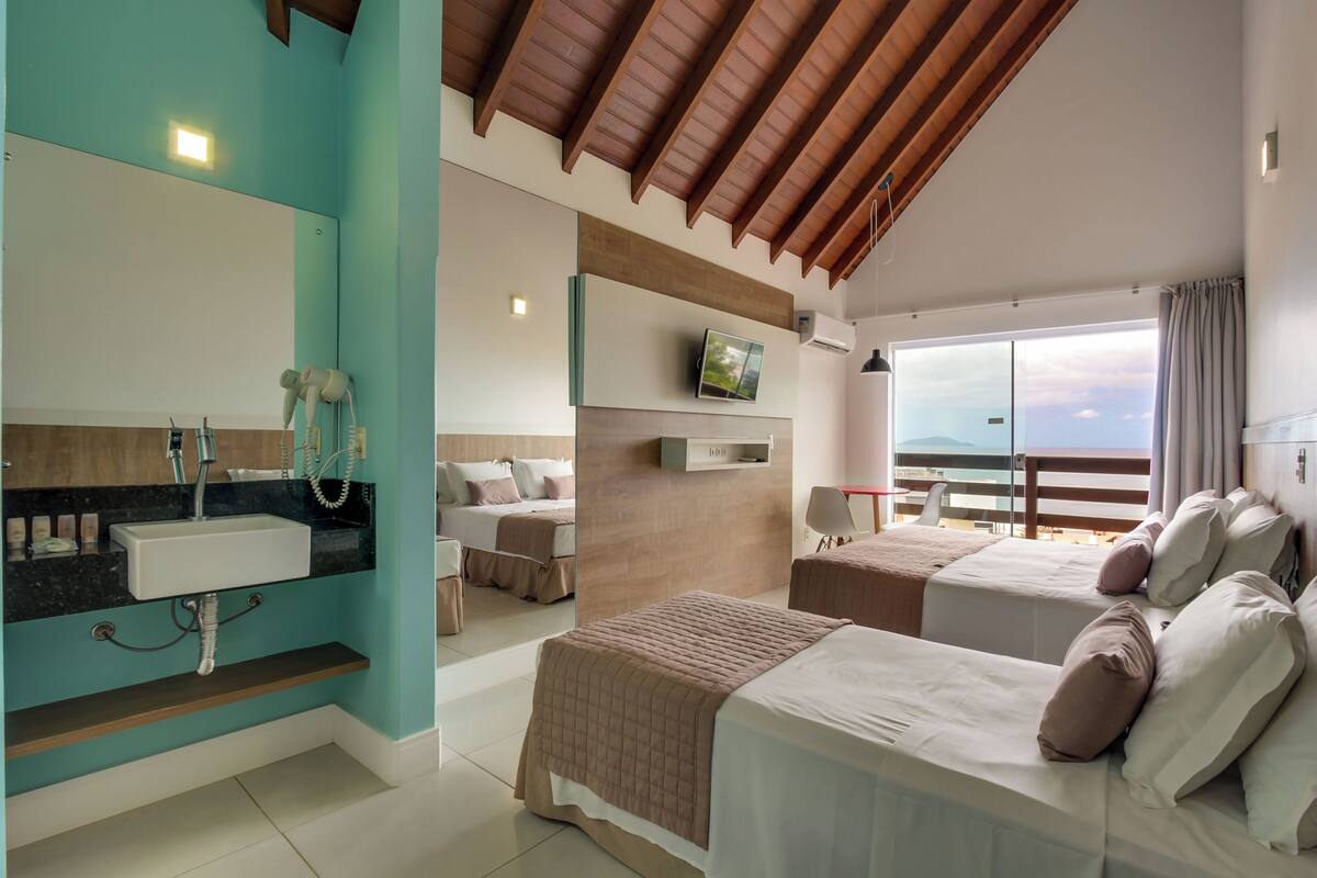 A modern hotel room with a large mirror, a sink, a television, a bed, and a balcony with a view.