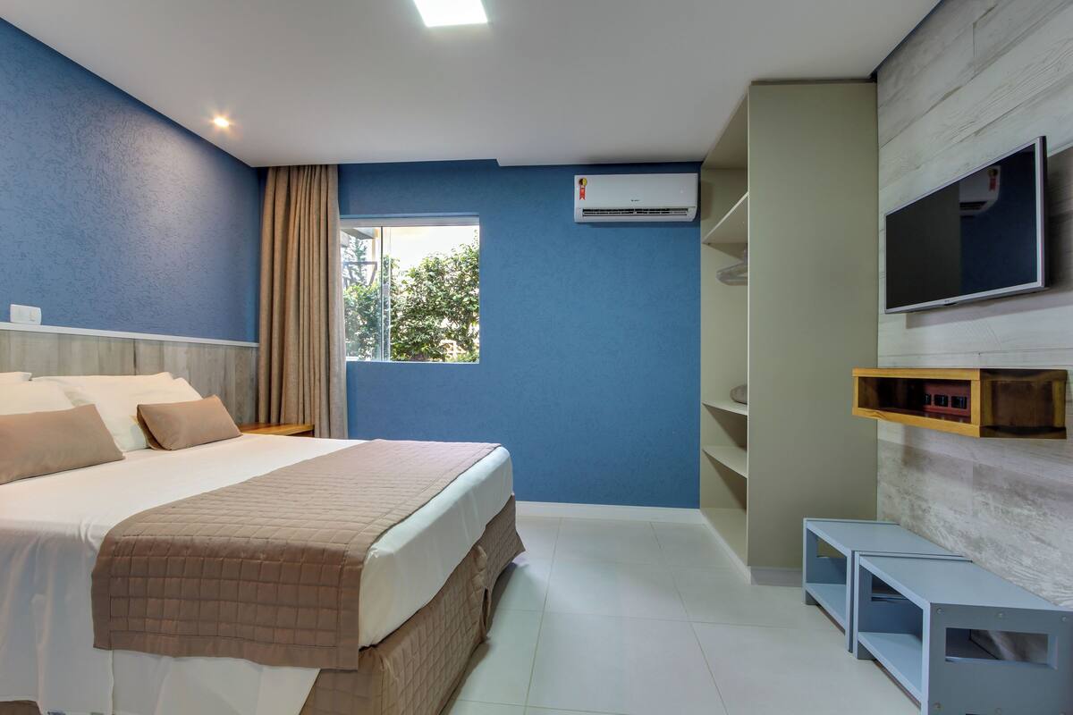A modern hotel room with a large bed, a TV mounted on the wall, and a window with curtains.