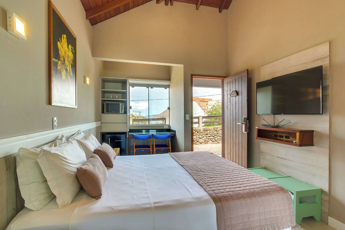 A bedroom with a large bed, a desk with two chairs, a television, and a view of the outside.