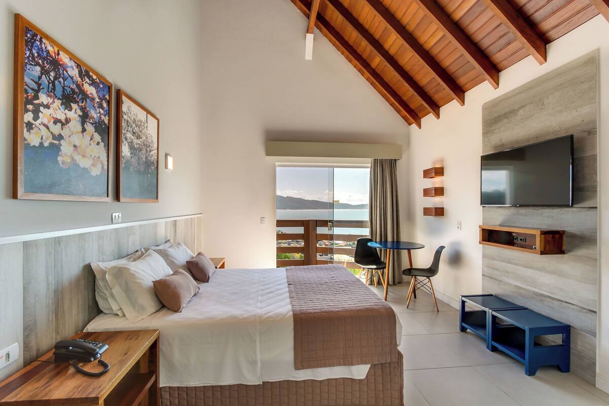 A hotel room with a bed, a desk, a chair, a TV, and a balcony with a view.