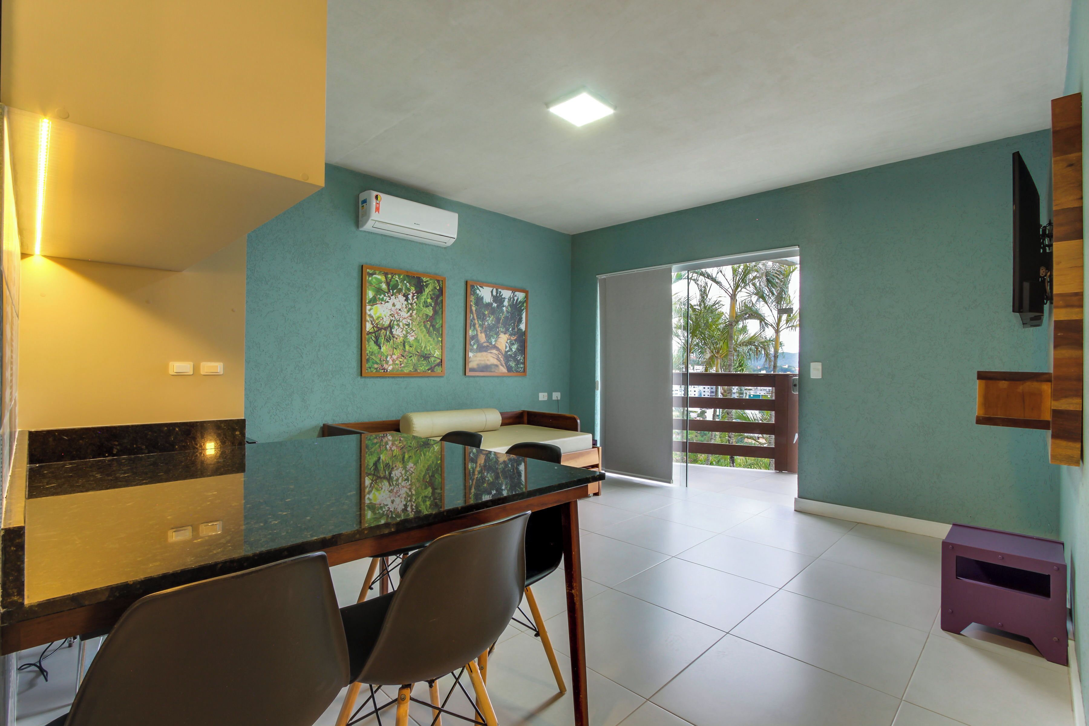 Amplia sala de estar con mesa de comedor, sillas y sofá. Hay una puerta corrediza de vidrio que da a un balcón con vistas a palmeras.