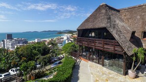 Un hotel con techo de paja, amplias ventanas y vistas a la playa y al océano.