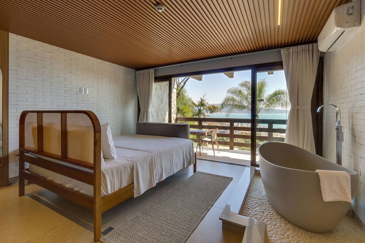 A bedroom with a wooden bed, a bathtub, and a balcony with a view.