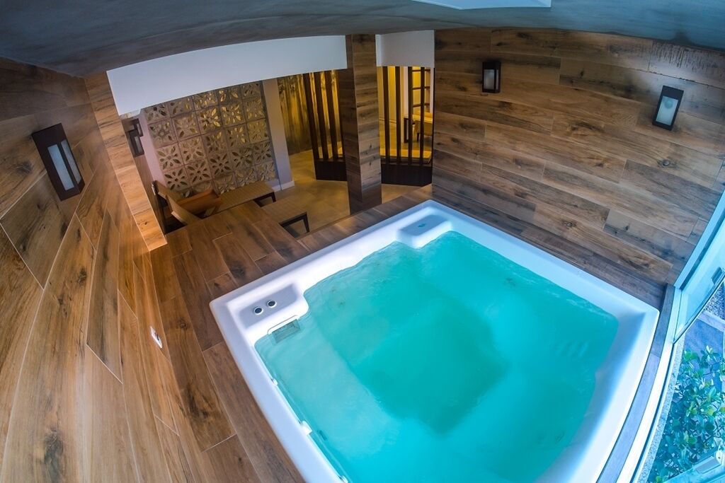 A modern interior with a large, rectangular hot tub in the center, surrounded by wooden flooring and walls.