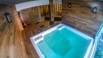 A modern interior with a large, rectangular hot tub in the center, surrounded by wooden flooring and walls.