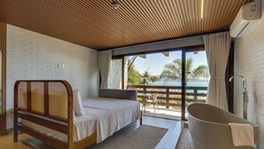 Un dormitorio con cama, una bañera grande y un balcón con vistas a palmeras.
