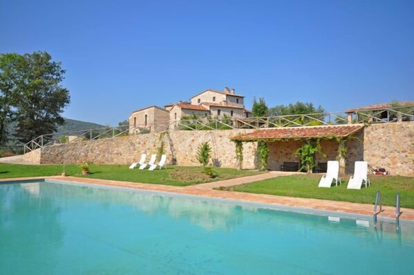 Una piscina con sillas de descanso y un muro de piedra.