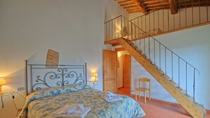 A bedroom with a bed, a wooden staircase, a chair, and a nightstand with a lamp.