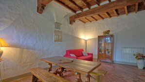 A rustic room with exposed wooden beams, a red sofa, a wooden table with benches, a lamp, and a cabinet with glass doors.