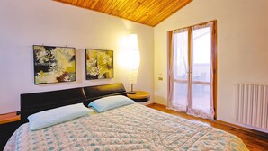 Ein Schlafzimmer mit einem Bett, zwei an der Wand befestigten Bildern, einer Nachttischlampe und einem Fenster mit Spitzenvorhängen.