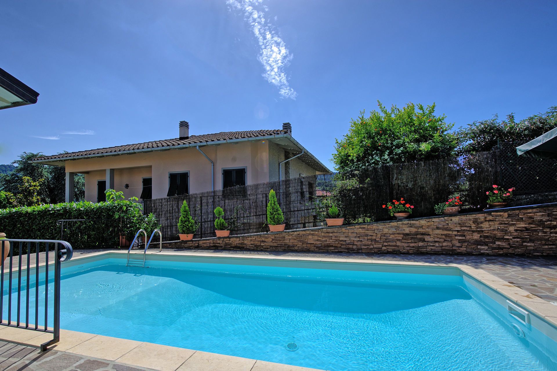 A swimming pool with a stone wall and potted plants.