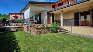 Ein zweistöckiges Haus mit überdachter Terrasse, Steintreppe und Swimmingpool.