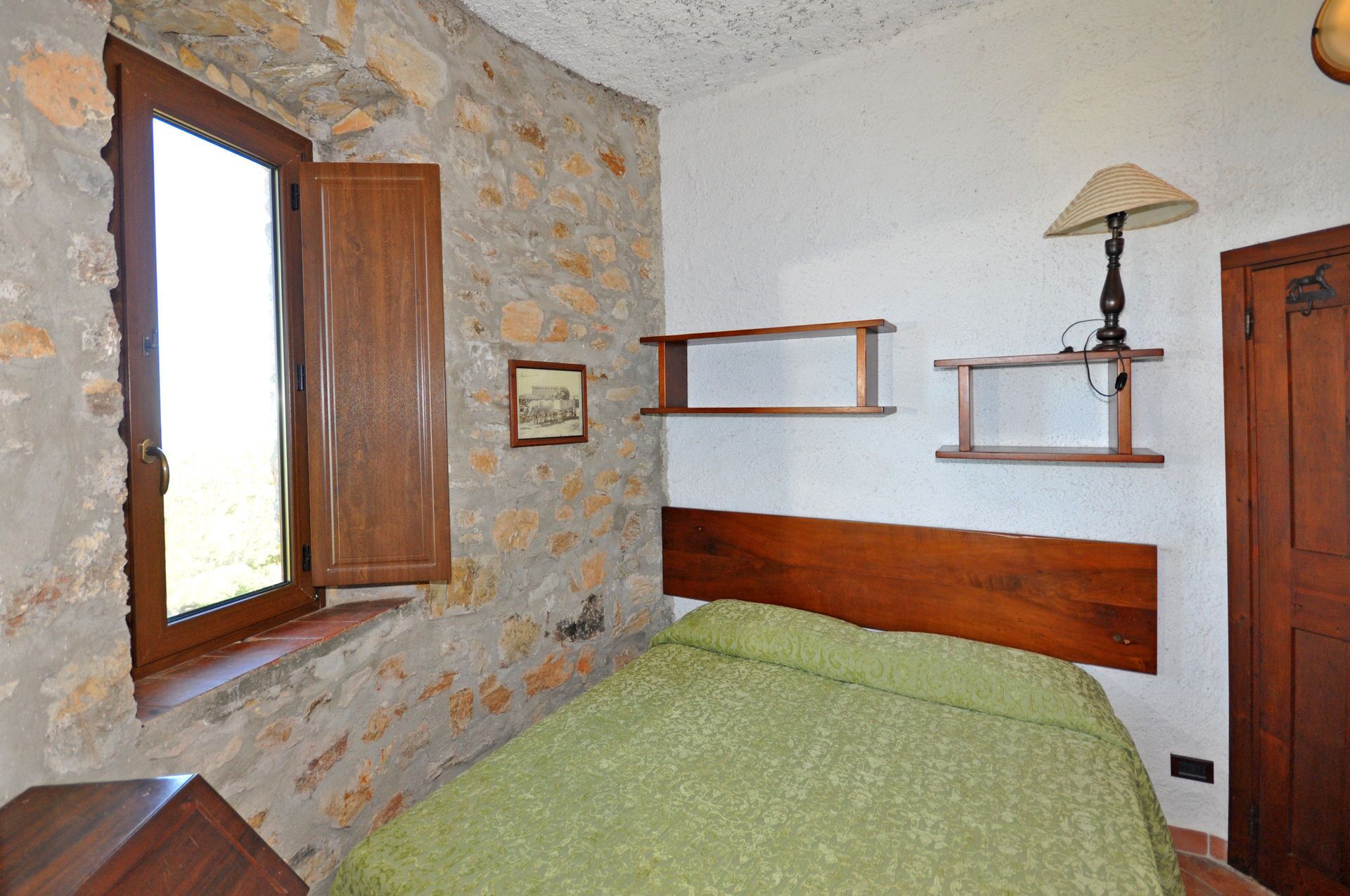 Une chambre avec un mur en pierre, une tête de lit en bois et une fenêtre avec un cadre en bois.