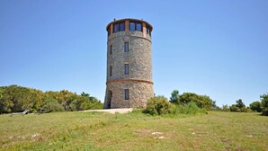 Een stenen toren met een ronde top, omringd door een grasveld en bomen.